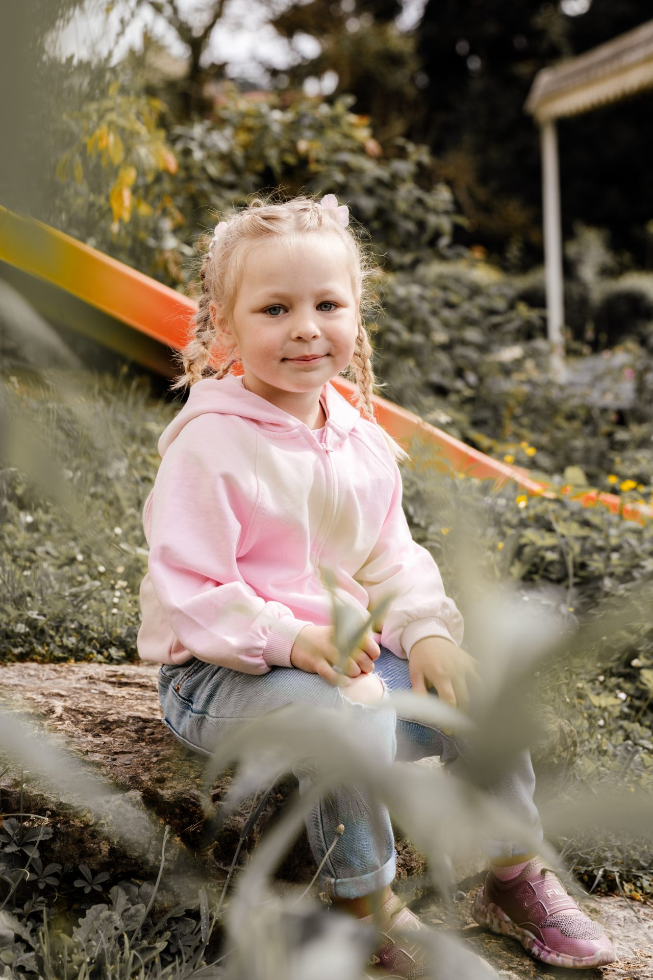 Mädchen im rosa Hoodie sitzt beim Kindergarten-Fotoshooting vor einer Rutsche