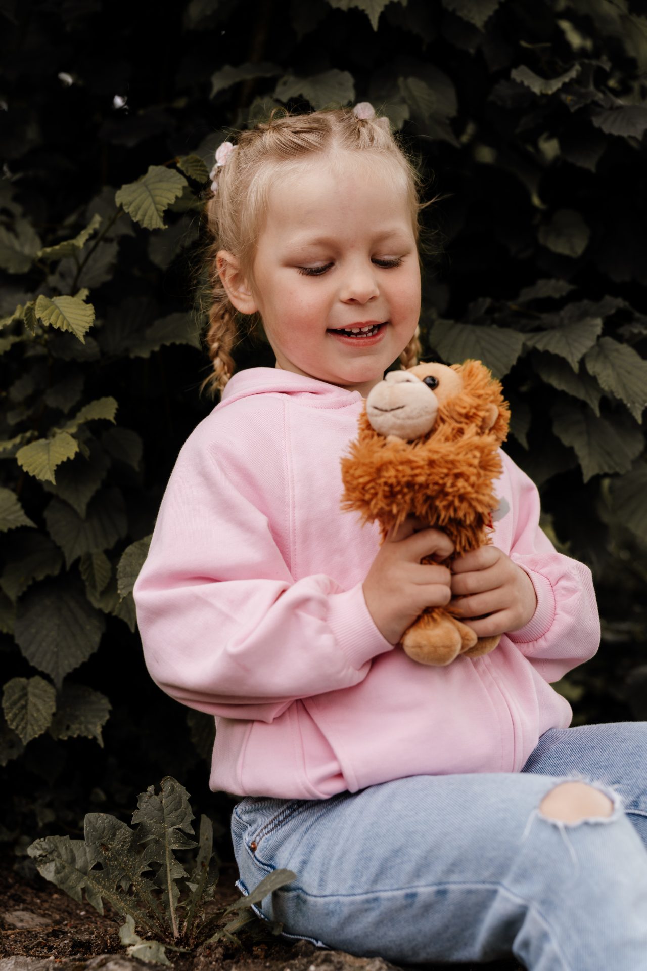 Mädchen sitzt im Garten und hält lachend ihr Stofftier fest