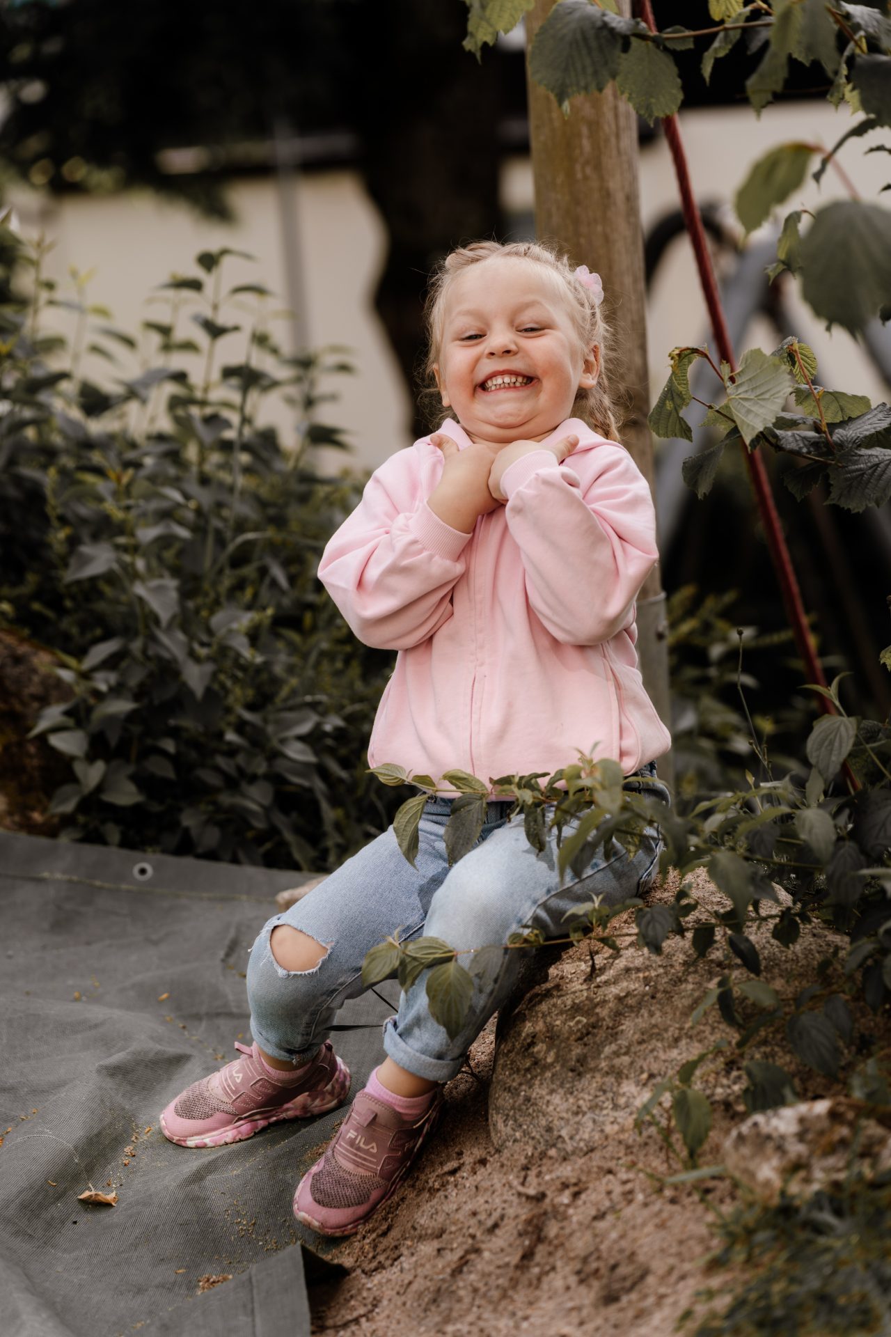 Lachendes Mädchen mit Zöpfen hält die Hände ans Kinn beim Kindergarten-Fotoshooting