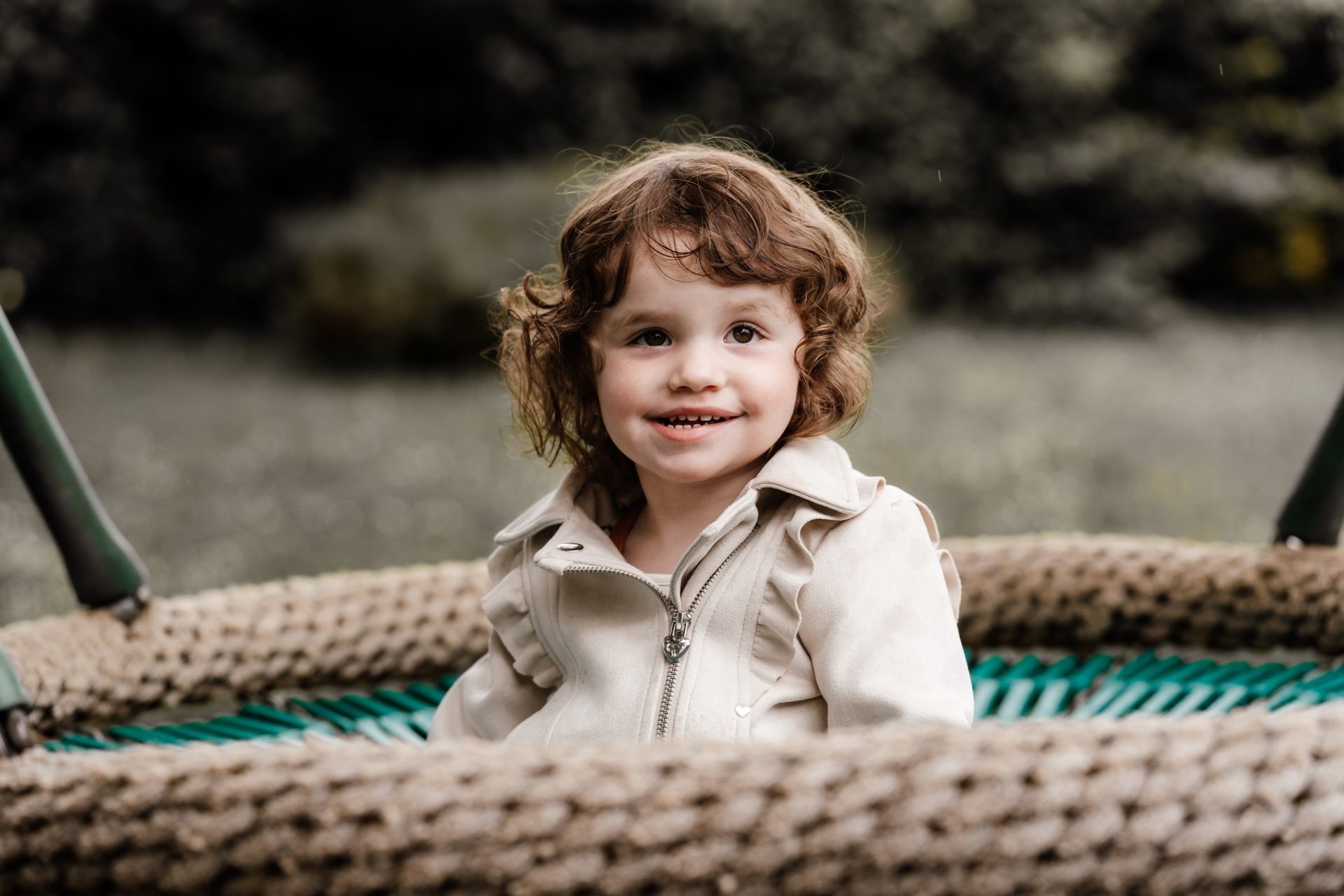 Mädchen in heller Jacke sitzt strahlend in einer Nestschaukel