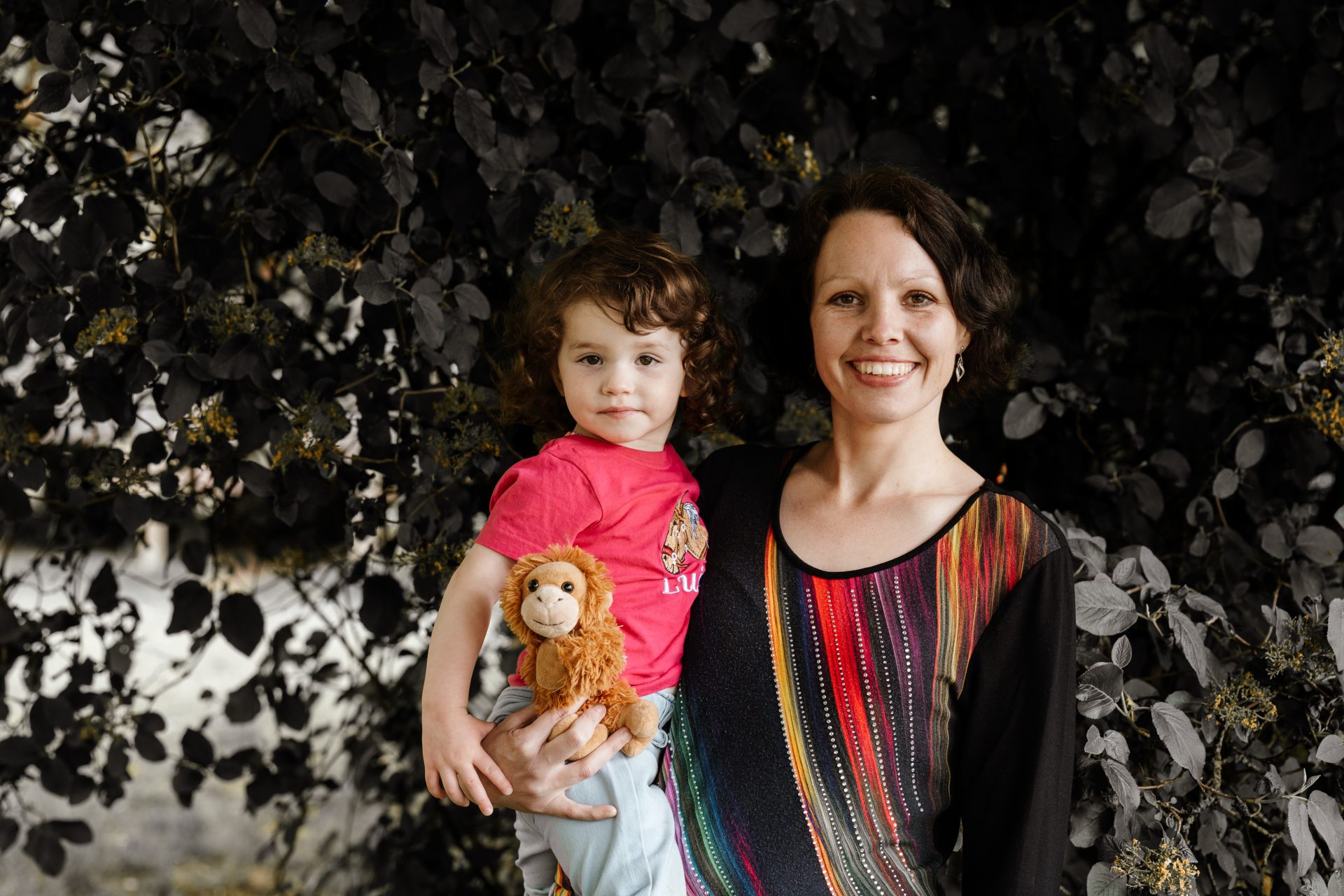 Mutter steht neben ihrer Tochter im pinken Shirt mit Kuscheltier