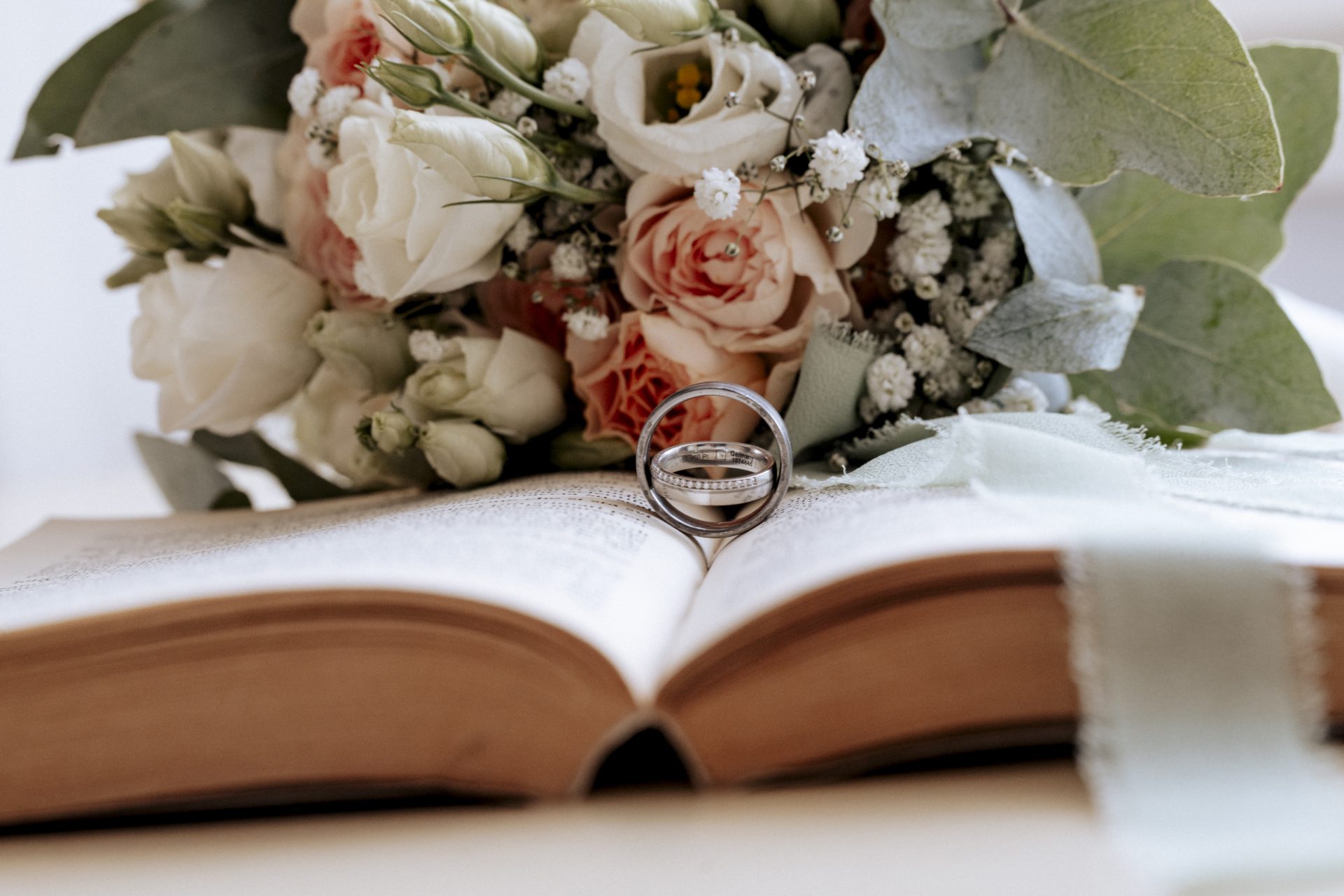 Eheringe auf einem aufgeschlagenen Buch vor dem Brautstrauß aus Rosen und Eukalyptus