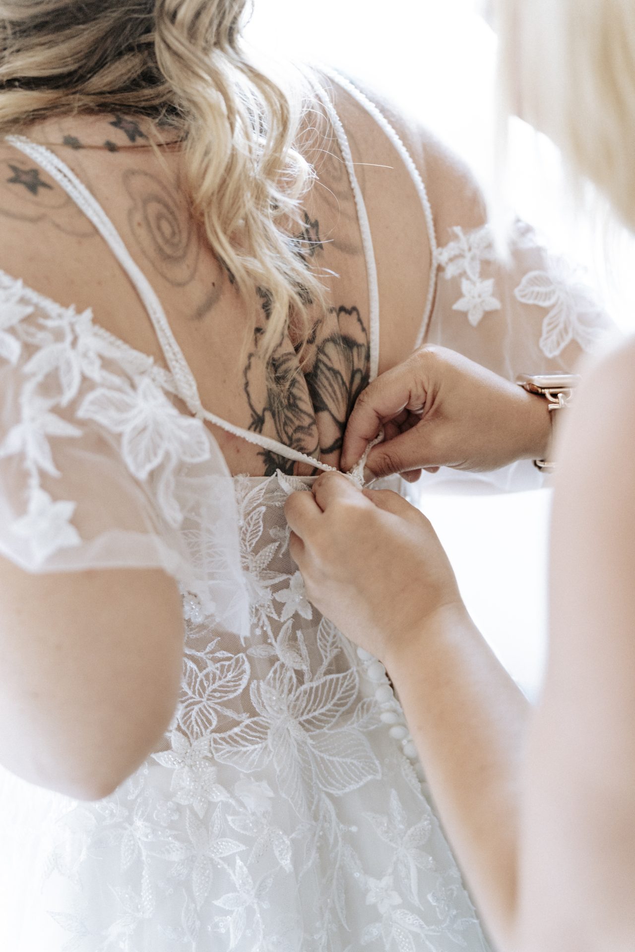 Helfende Hände schließen das Spitzenkleid am Rücken der Braut