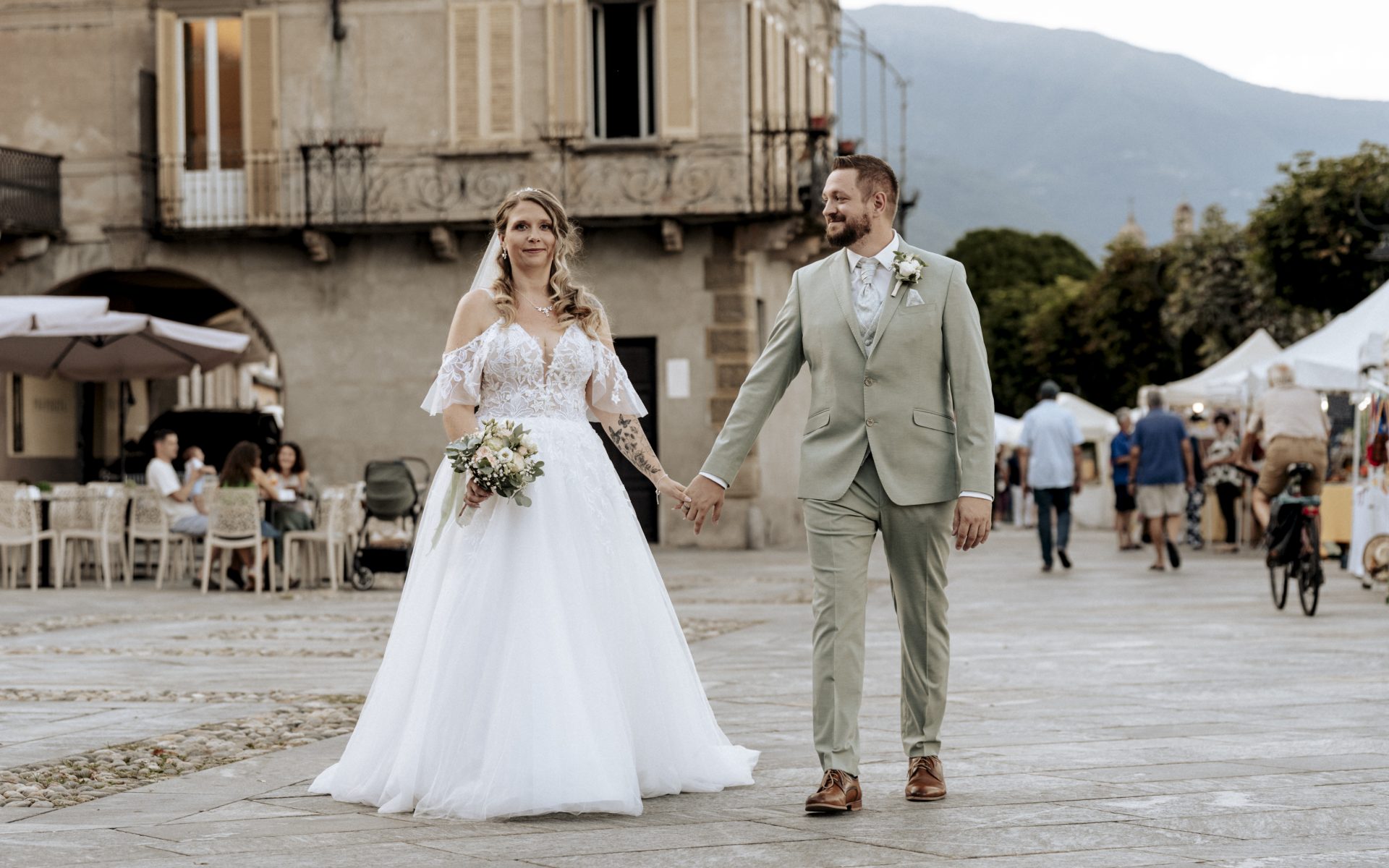 Brautpaar überquert Hand in Hand die belebte Piazza am Lago Maggiore