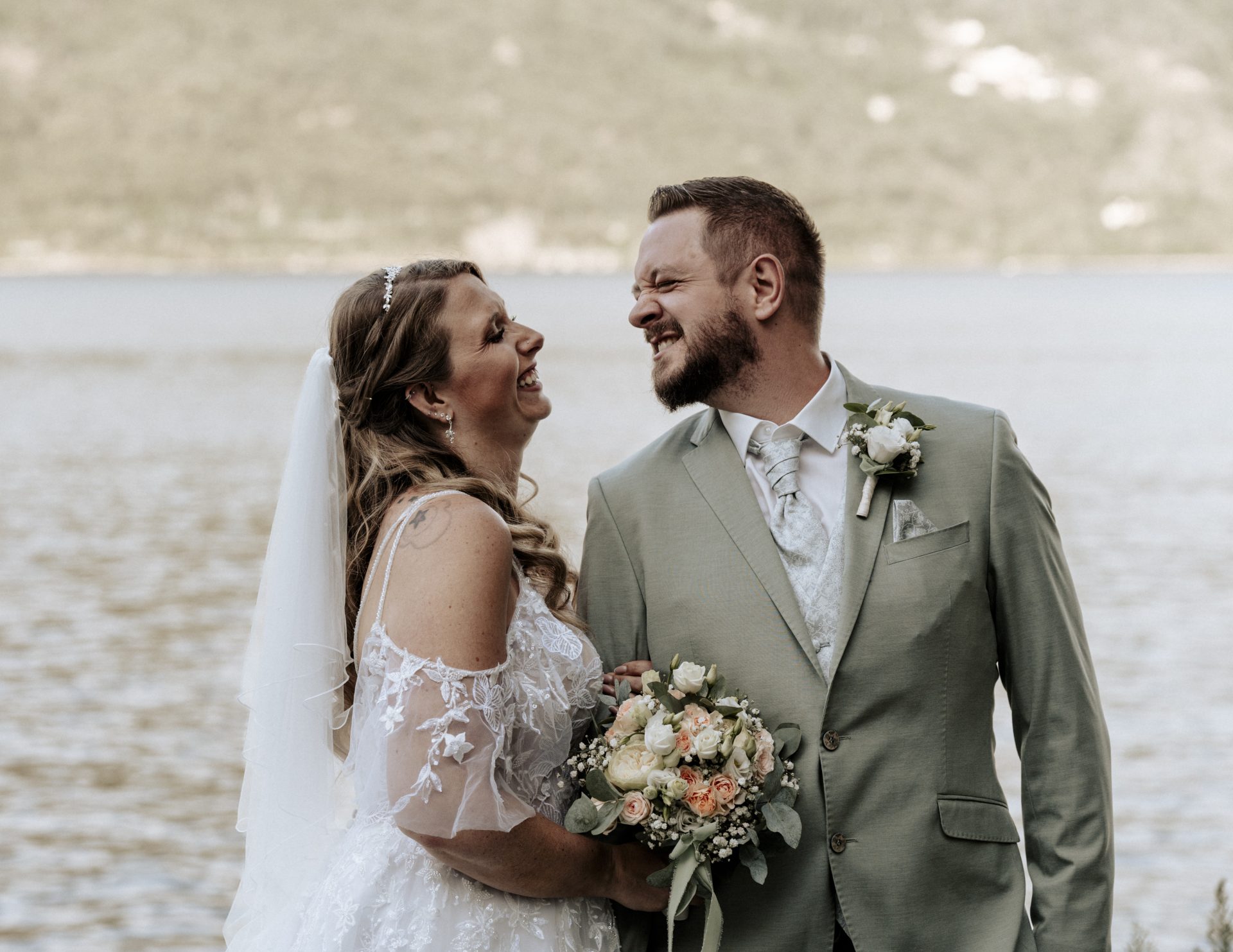 Braut und Bräutigam lachen sich vor dem glitzernden See herzlich an